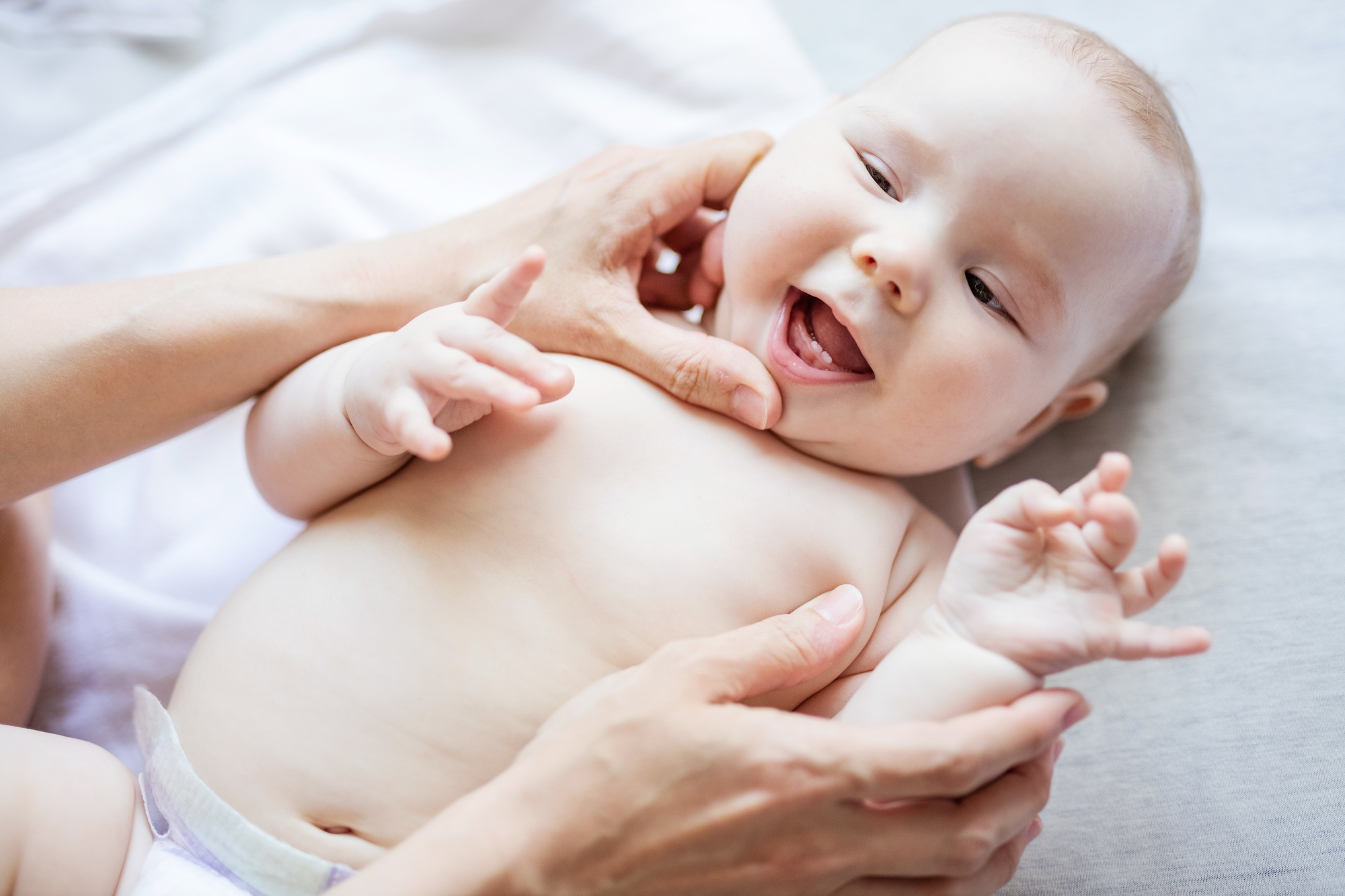 Cute baby girl lying on bed while mother looking at her first teeth