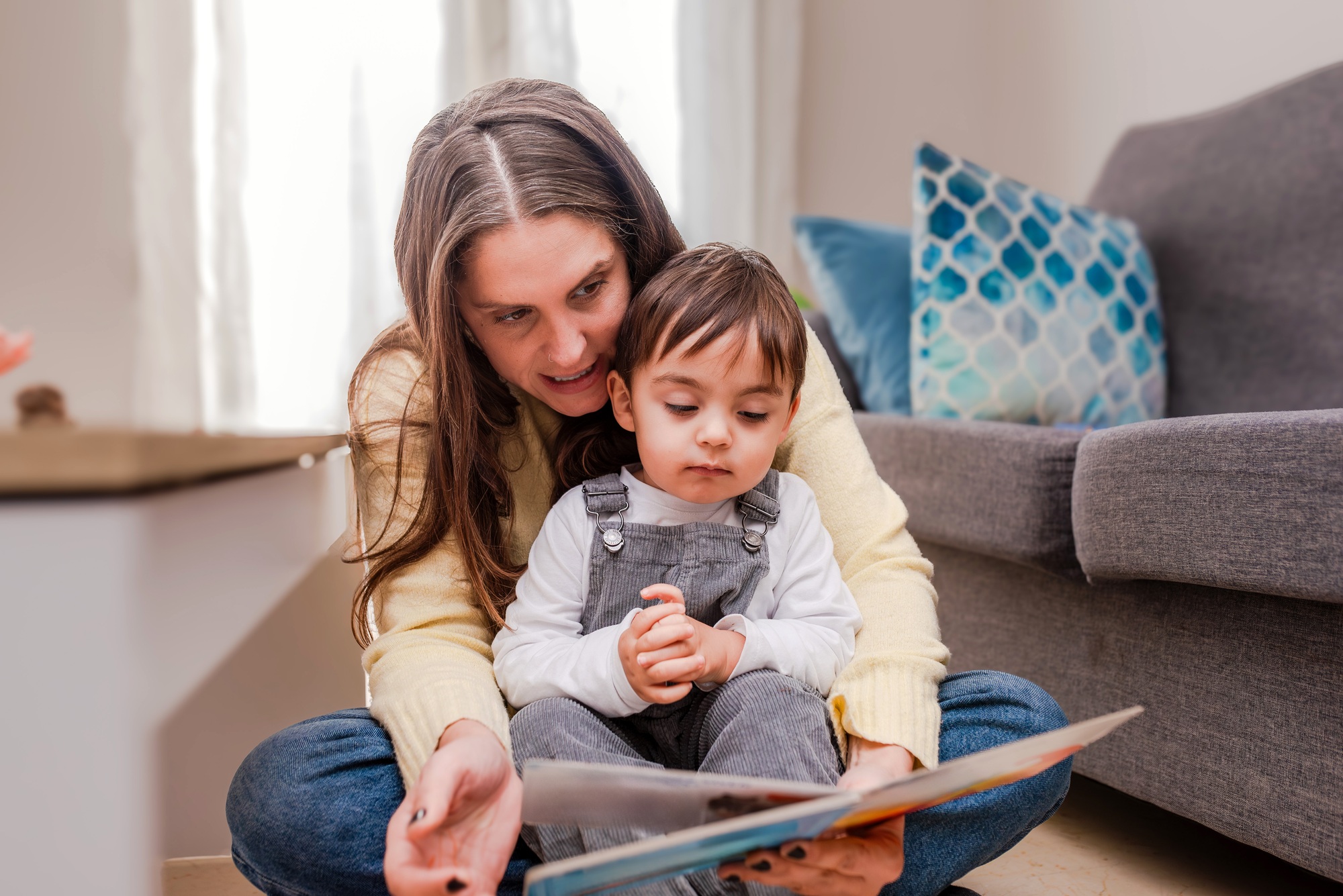 Toddler Boy Listening to Mother Reading a Storybook sitting on the floor at home